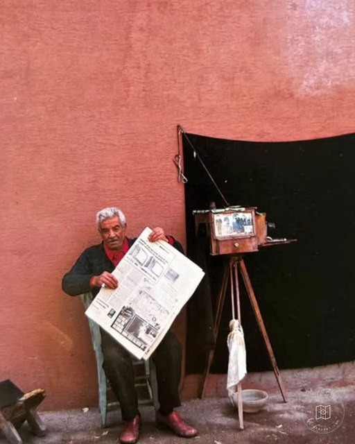 A man with a newspaper beside a bellows camera
