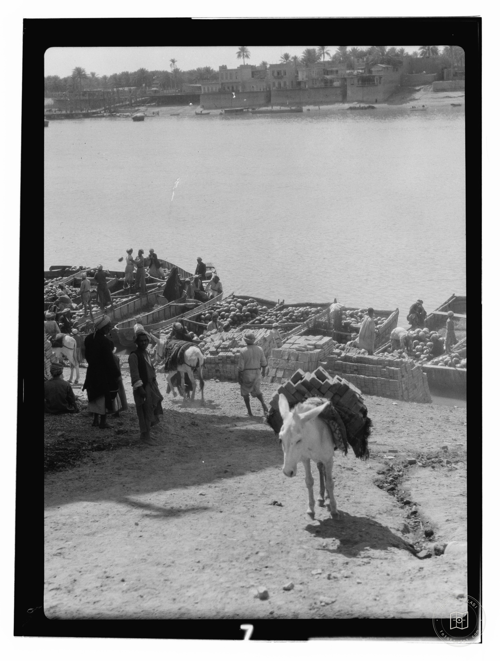 boats being unloaded at river with city in background